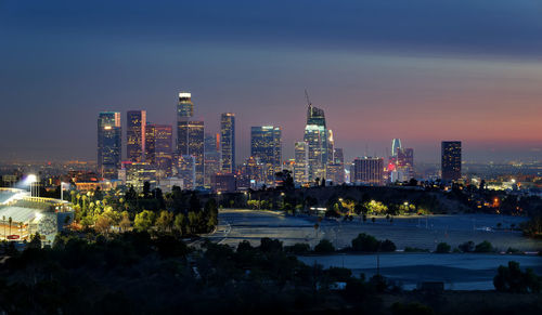 Illuminated buildings in city against sky at dusk