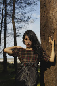 Young woman standing by tree trunk in forest