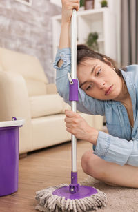 Tired woman holding broom while sitting on floor at home