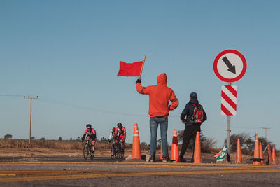 People standing by road against clear blue sky