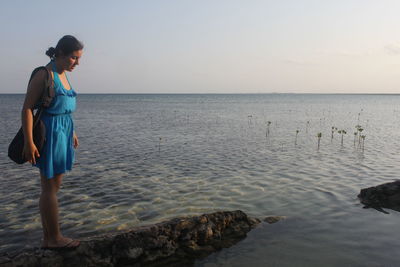 Young woman standing on rock by sea against sky