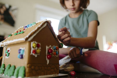 Low angle view of girl making gingerbread house on table at home