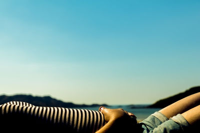 Midsection of woman lying on back against clear blue sky