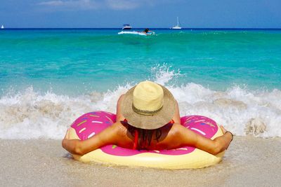 Rear view of young woman with inflatable ring relaxing at beach during sunny day