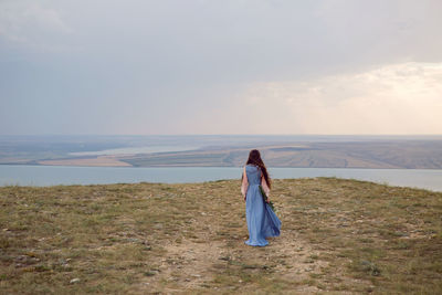 Woman stands on a mountain cliff in a blue long dress in summer