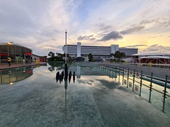 View of swimming pool by buildings against sky at sunset