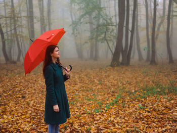 Young woman looking away while standing in autumn tree