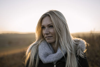 Portrait of young woman with arms outstretched against sky during sunset
