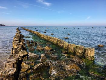 Wooden posts and stones in sea against sky