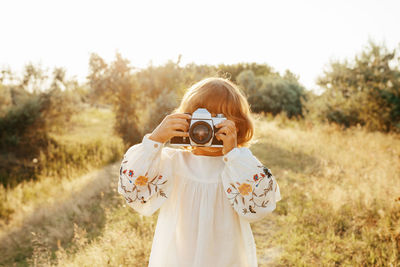 Portrait of boy holding camera while standing on field