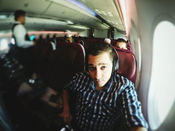 Portrait of man wearing headphones traveling in airplane on sunny day