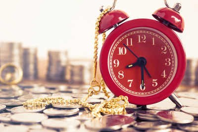 Close-up of alarm clock on coins with gold chain at table