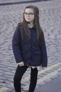 Girl wearing eyeglasses and jacket standing on cobbled street