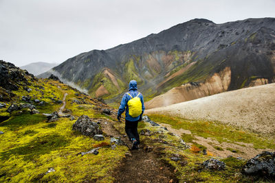 Rear view of man walking on mountain against sky