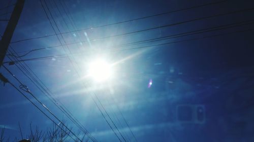 Low angle view of power lines against bright sky