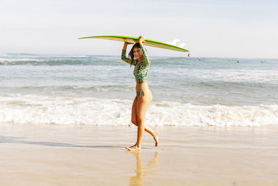 Young woman carrying surfboard while walking on shore at beach