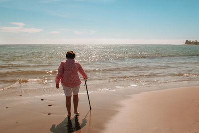 Rear view of woman walking with cane at beach