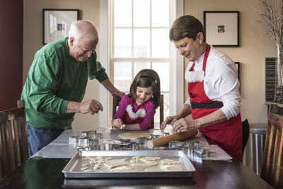 Cute granddaughter making gingerbread cookies with grandparents at home