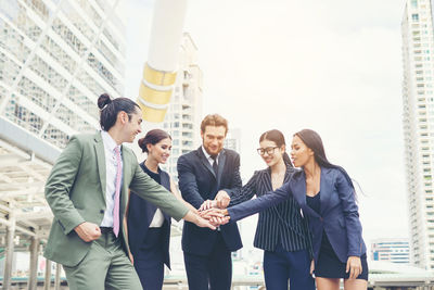 Smiling young colleagues stacking hands on footpath in city