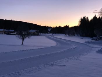 Snow covered land against sky during sunset