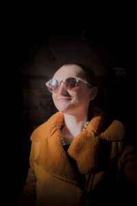 Smiling young woman wearing sunglasses and coat at home