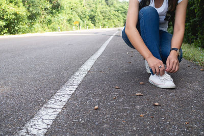 Low section of woman tying shoelace on road