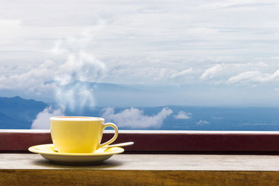 Close-up of coffee cup on window sill against mountains