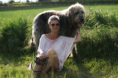 Confident mature woman with hairy dog sitting on grassy field