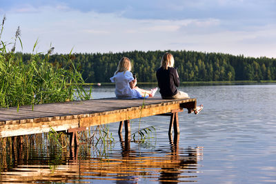 Rear view of people sitting by lake against sky