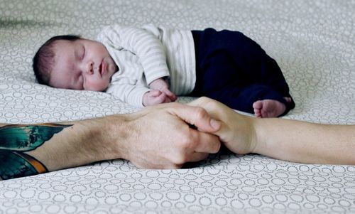 Close-up of couple holding hands while baby sleeping on bed