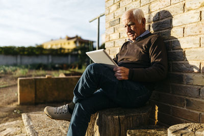 Senior man sitting on tree stump using tablet