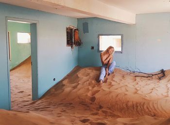 Topless woman sitting on sand in abandoned room at kolmanskop