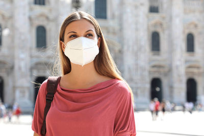 Close-up of woman wearing mask standing against building in city