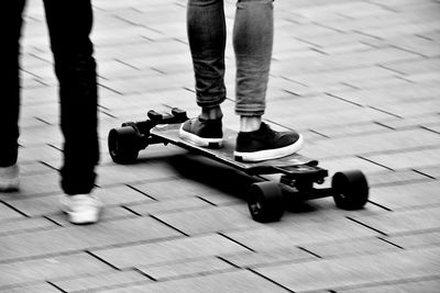 Low section of man walking with friend skateboarding on street