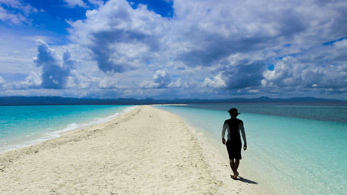 Rear view of man walking on beach against sky