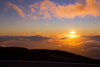 Scenic view of dramatic sky over silhouette landscape during sunset