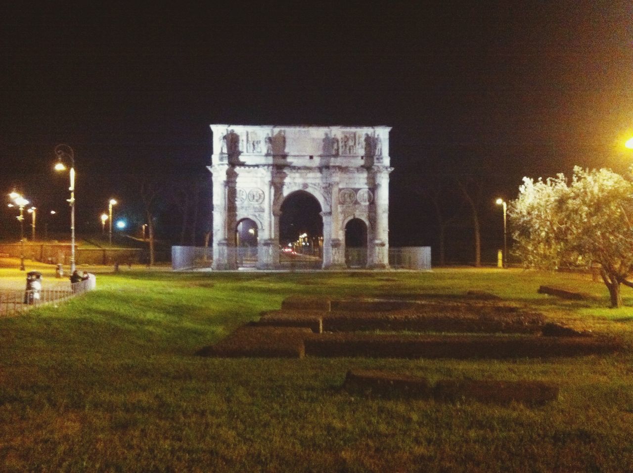 architecture, built structure, grass, night, arch, illuminated, building exterior, lawn, green color, tree, park - man made space, street light, clear sky, history, outdoors, sky, incidental people, travel destinations, city, architectural column