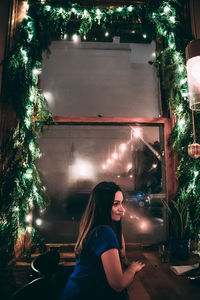 Side view of thoughtful woman sitting against window in restaurant during christmas