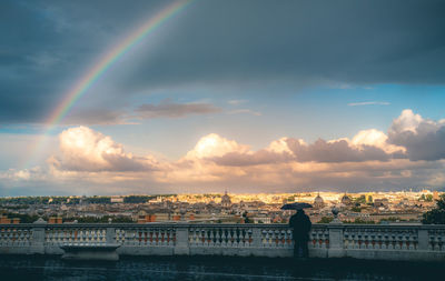 Rainbow over cityscape against sky during sunset