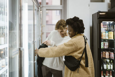 Multiracial couple buying drinks from refrigerated section while shopping at supermarket