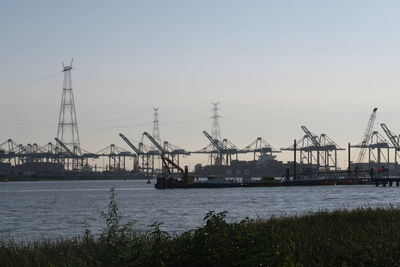 Cranes at harbor against sky