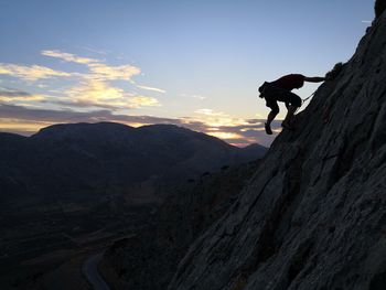 Side view of man rope climbing mountain against sky during sunset