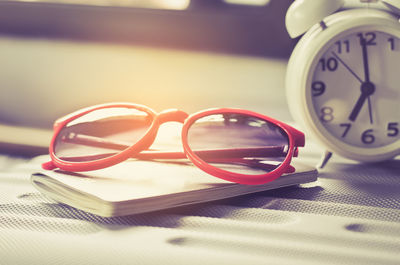 Close-up of sunglasses with book and alarm clock on table