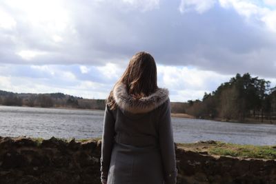 Rear view of woman looking at lake against cloudy sky