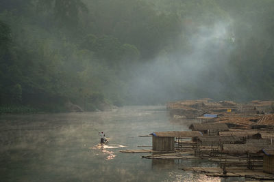 Man sailing wooden raft in river during foggy weather