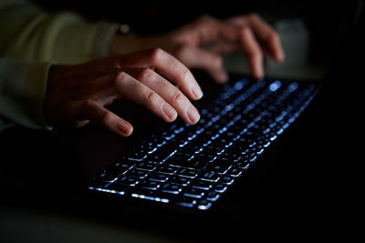 Typing on laptop keyboard at night, close up