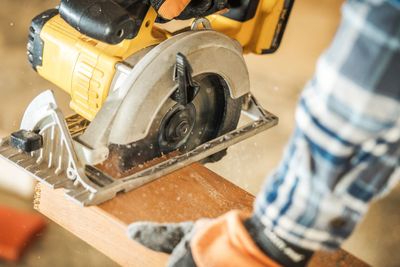 Cropped hand of carpenter cutting plank in workshop