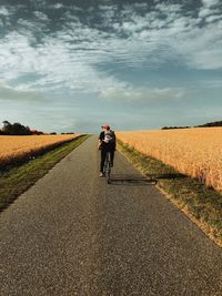 Rear view of man riding bicycle on road against sky