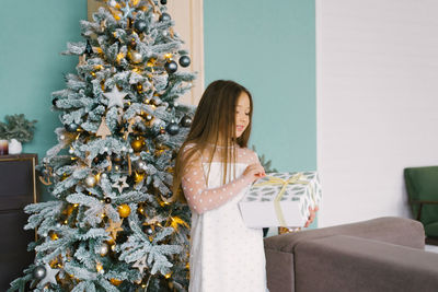 Excited curious little girl smiles as she opens christmas gift. beautifully decorated christmas tree