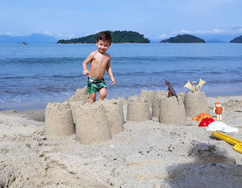 Shirtless boy making sandcastles at beach against sky